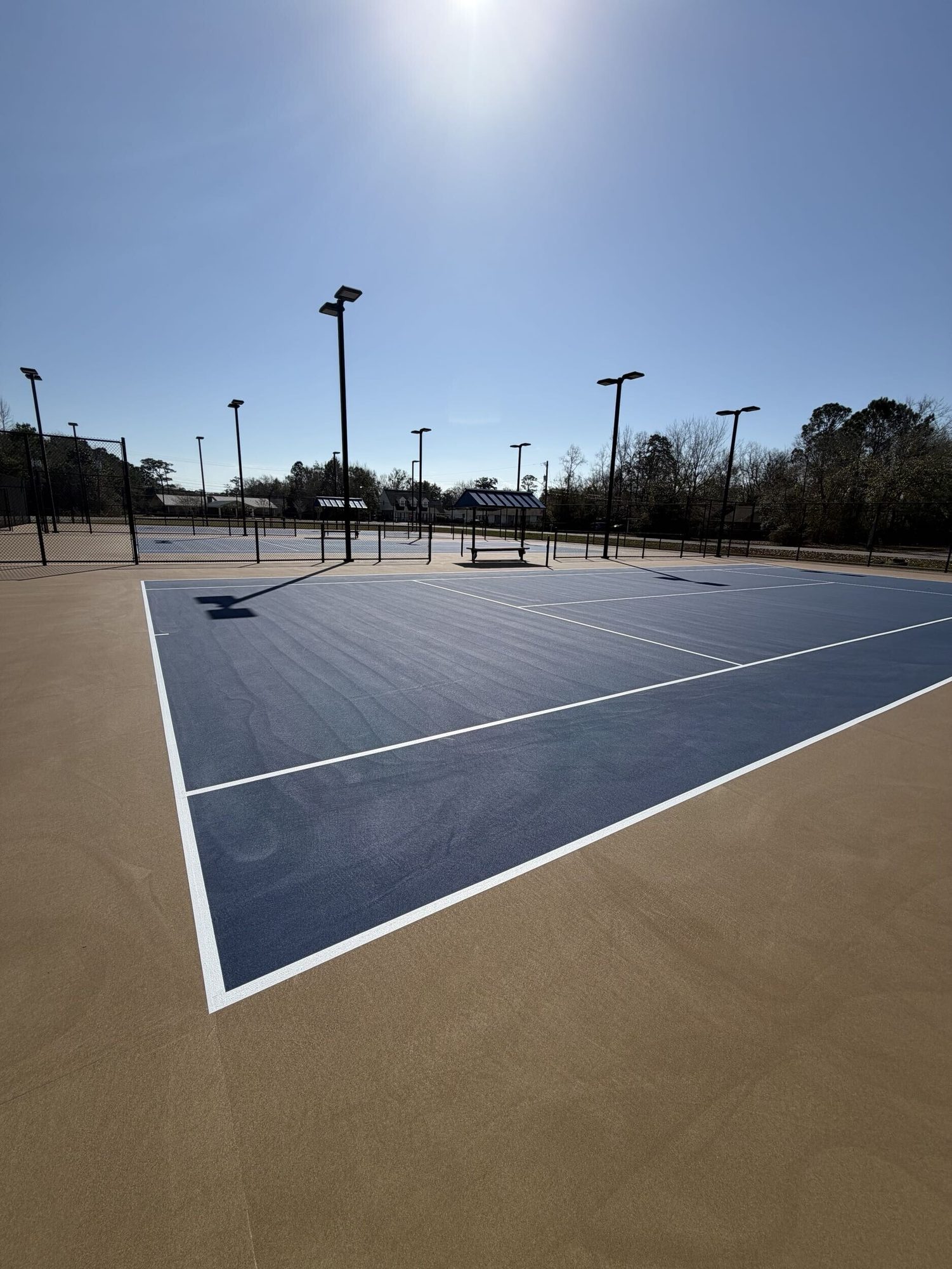 Corner of a resurfaced blue tennis court with fresh white lines at Bay High School in Bay St. Louis, MS