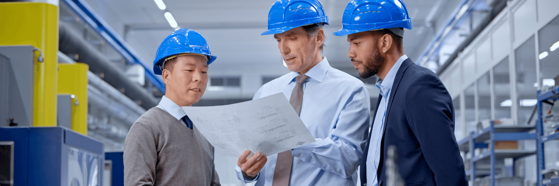 A diverse team of professionals gathered around a illuminated digital display table, reviewing technical diagrams and data in a collaborative work environment.