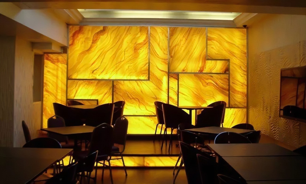 A modern dining area illuminated by backlit golden onyx panels, creating a warm and luxurious atmosphere.