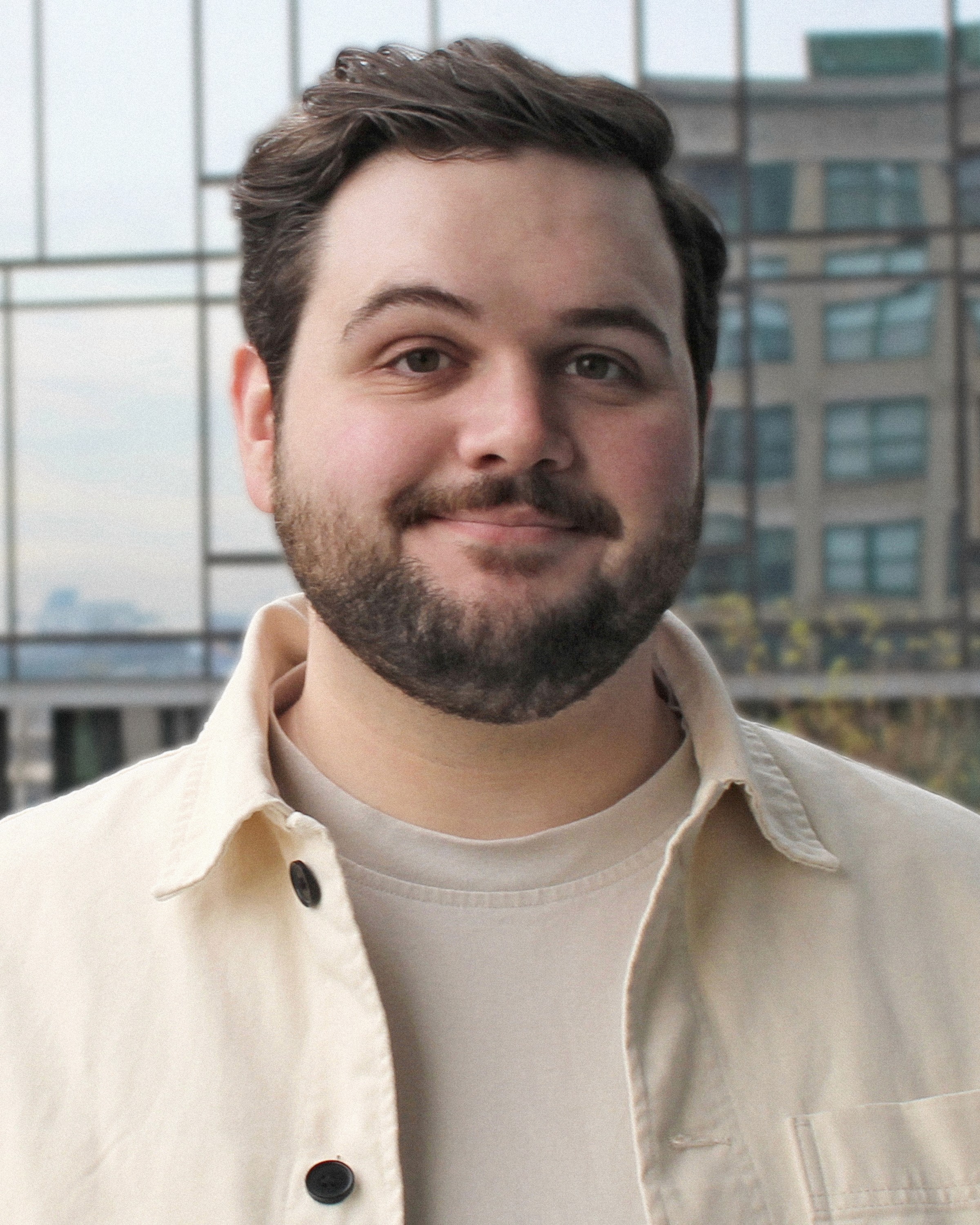 Person wearing a blue puffer jacket and red backpack standing in front of a light blue building on a city street.