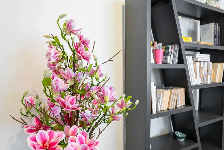 Pink magnolia blossoms beside a bookshelf of art supplies in the studio.