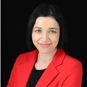 Kobieta z krótkimi czarnymi włosami w czerwonej marynarce i czarnej bluzce uśmiecha się, pozując na czarnym tle.