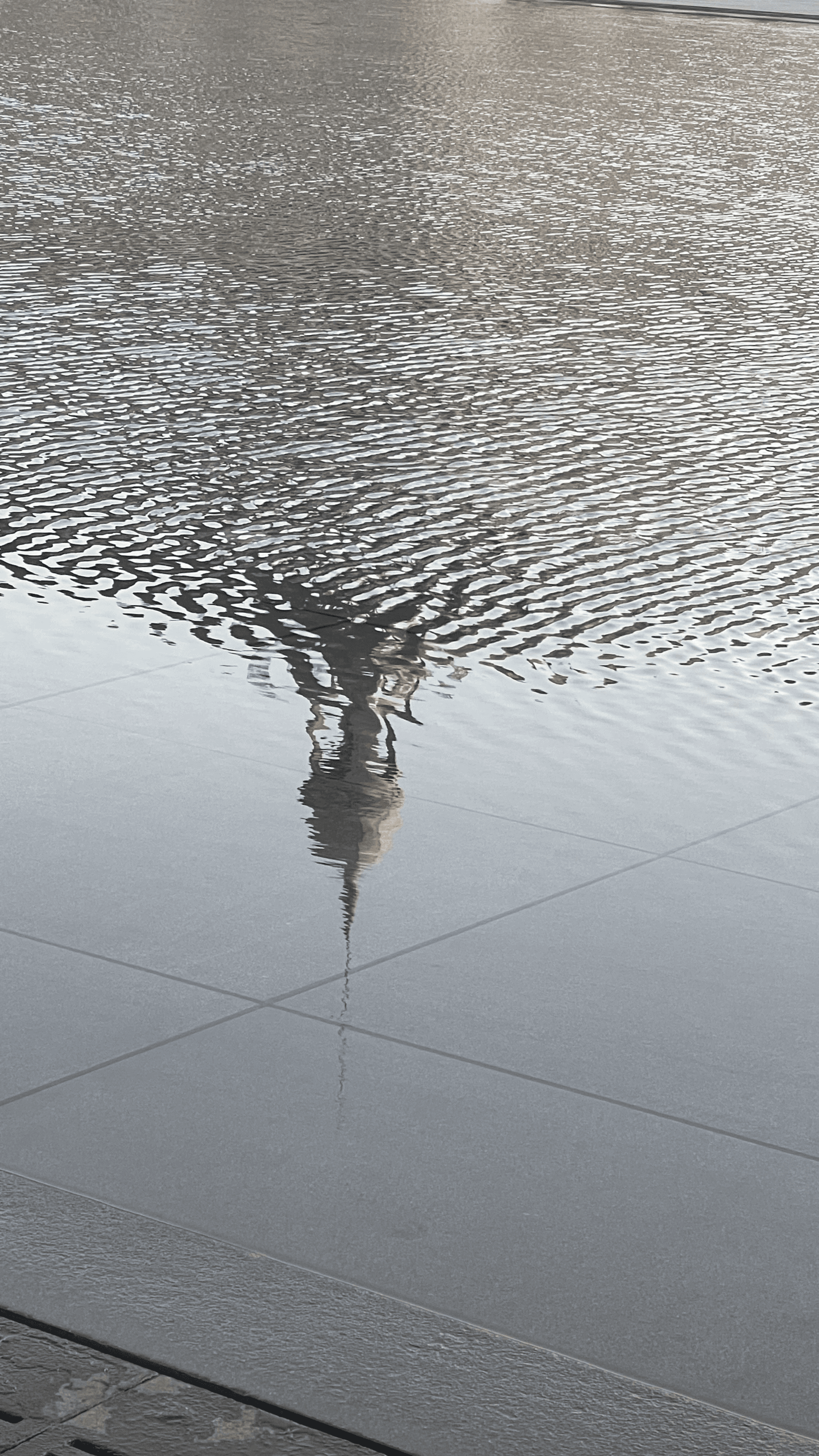 The reflection of a spire rippling across a shallow pool — abstract, poetic, and serene, merging architecture with water and motion.