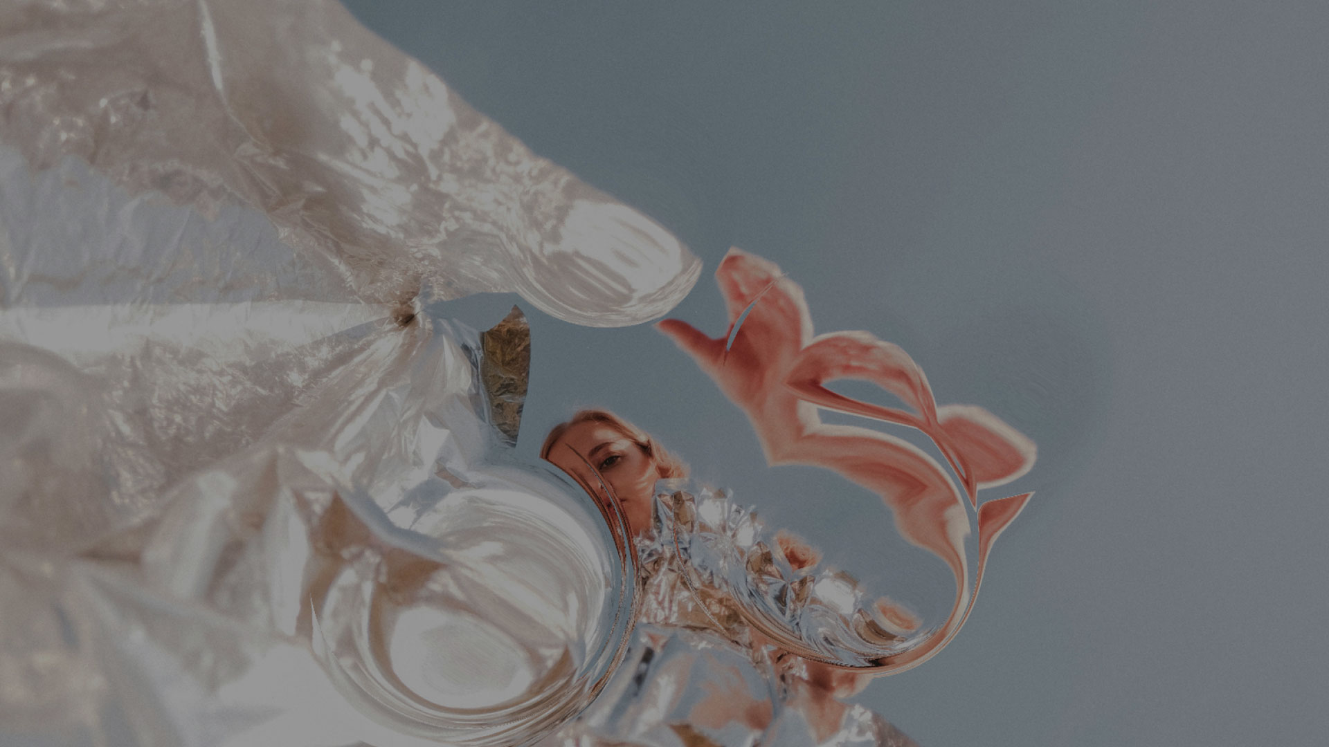 Close-up photo of a woman's hand holding a ring against a reflective surface, showing a distorted mermaid reflection.