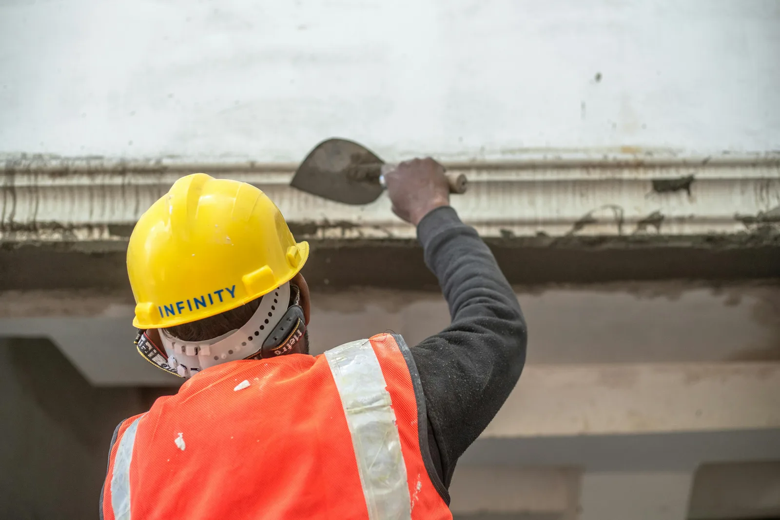 Construction worker in hard hat scraping concrete ceiling