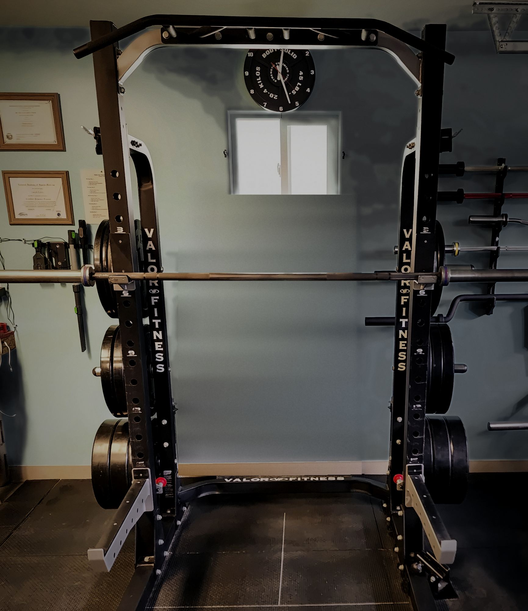 Half rack with bumper plates in Joseph's private Homer studio, with his framed training certificates on the wall