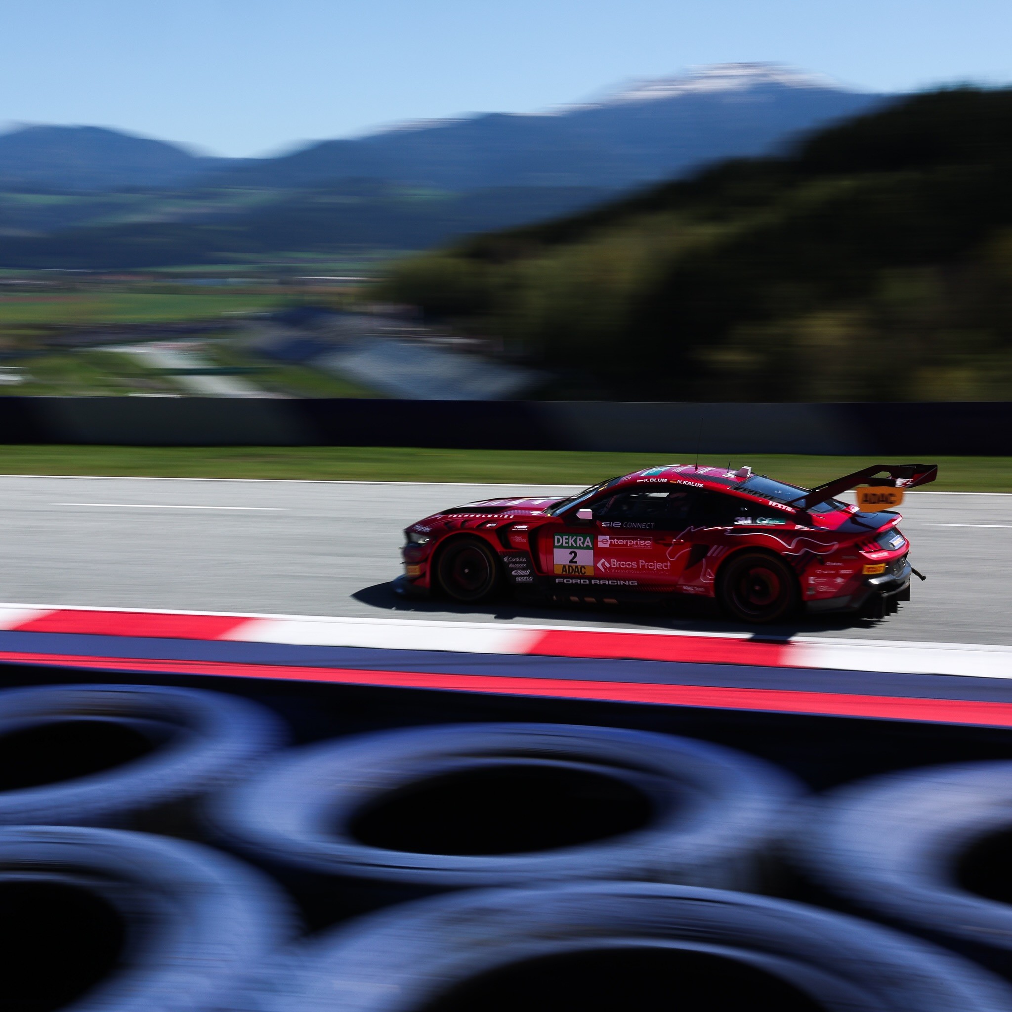 A red Ford Mustang GT3 race car speeding through a corner on a racetrack.