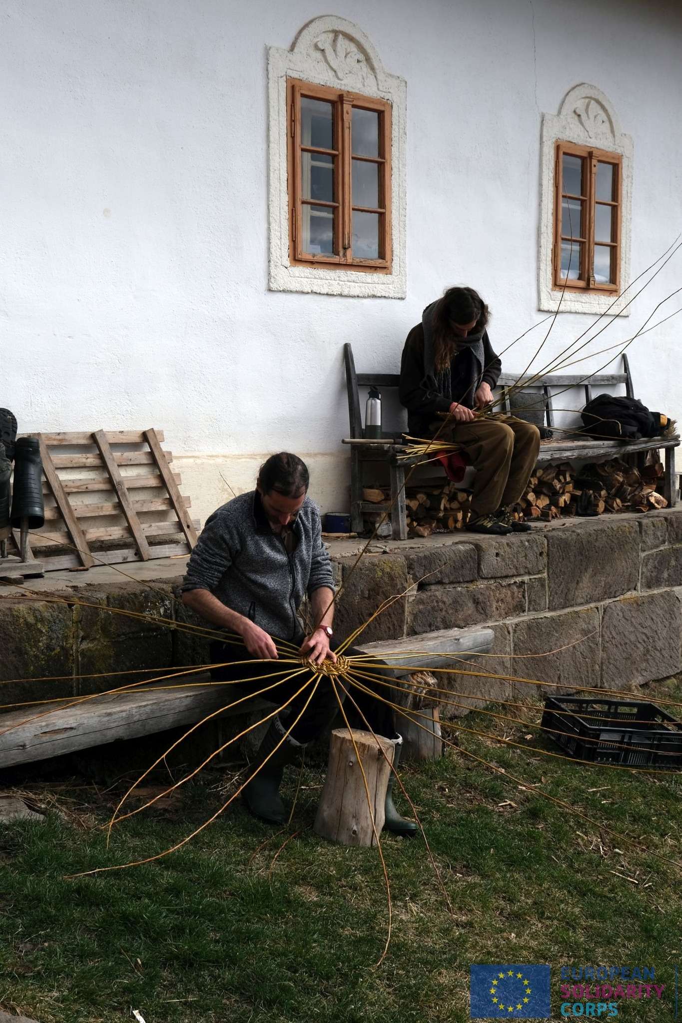 A young person with curly hair smiles at the camera while sitting in front of a laptop against a dark background.