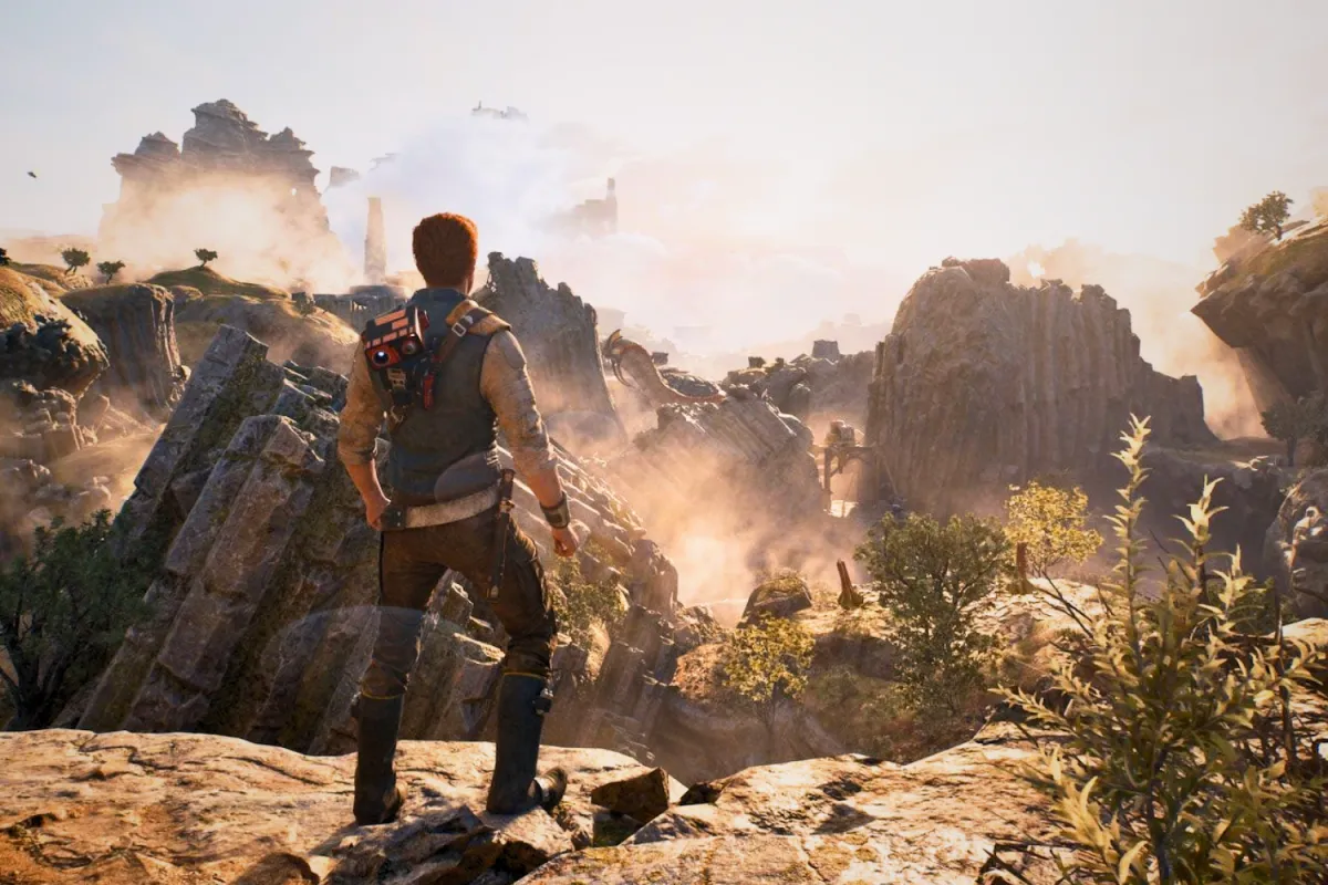 Cal Kestis stands on a rocky cliff, overlooking a vast, rugged landscape bathed in golden sunlight. BD-1, his loyal droid companion, is perched on his back as they take in the breathtaking view of towering rock formations, scattered trees, and remnants of ancient structures. The misty atmosphere and distant ruins hint at the challenges ahead in his journey through the Star Wars Jedi universe.