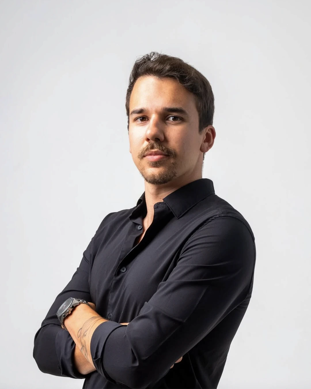 A smiling young woman in a pink blouse stands in an office setting, with soft lighting and a professional backdrop.