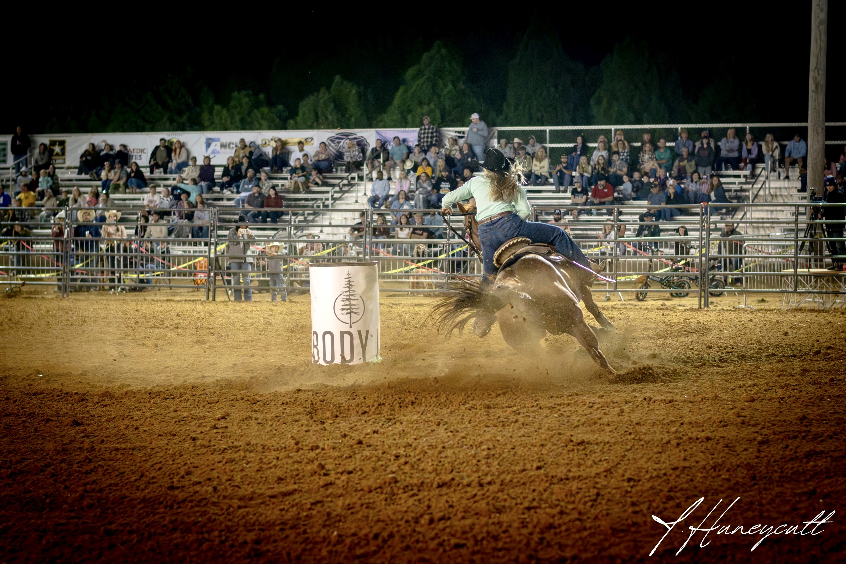 Rider and horse turning tightly around a barrel during a high-speed barrel racing run.