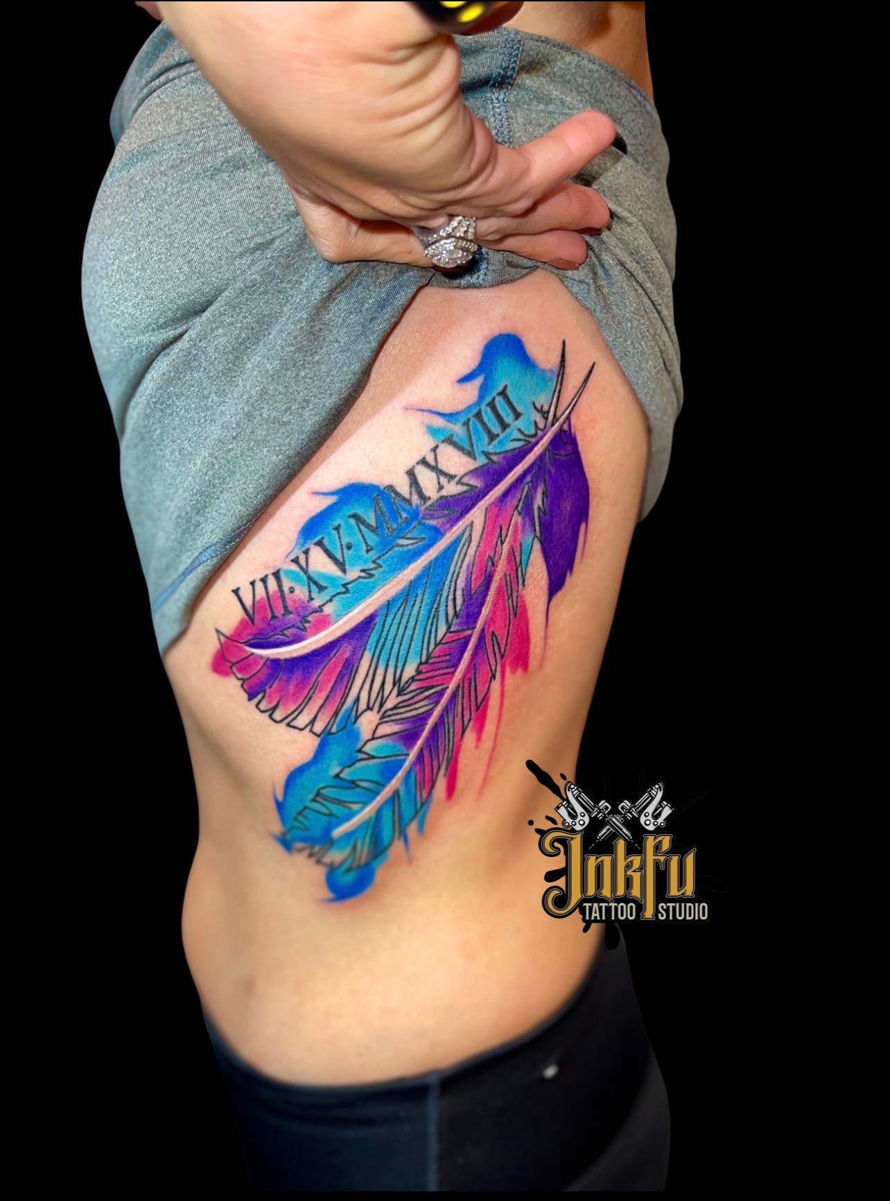 Color watercolor feather tattoo with a memorial date, by Meer Rich