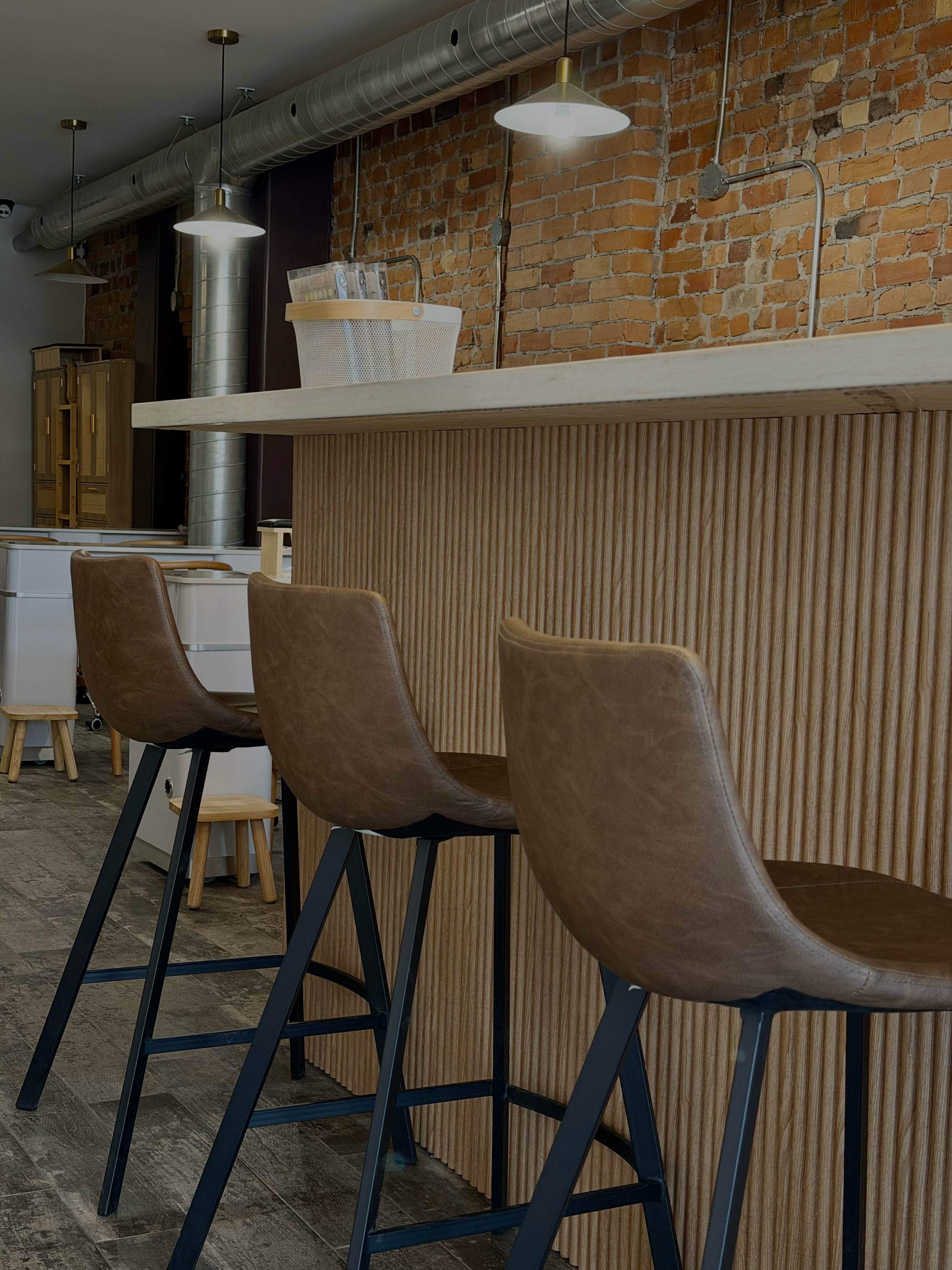 A cozy and inviting spa room with a neatly made bed, soft lighting, and warm wooden tones. The scene is partially framed by green plants, adding a natural and soothing touch.
