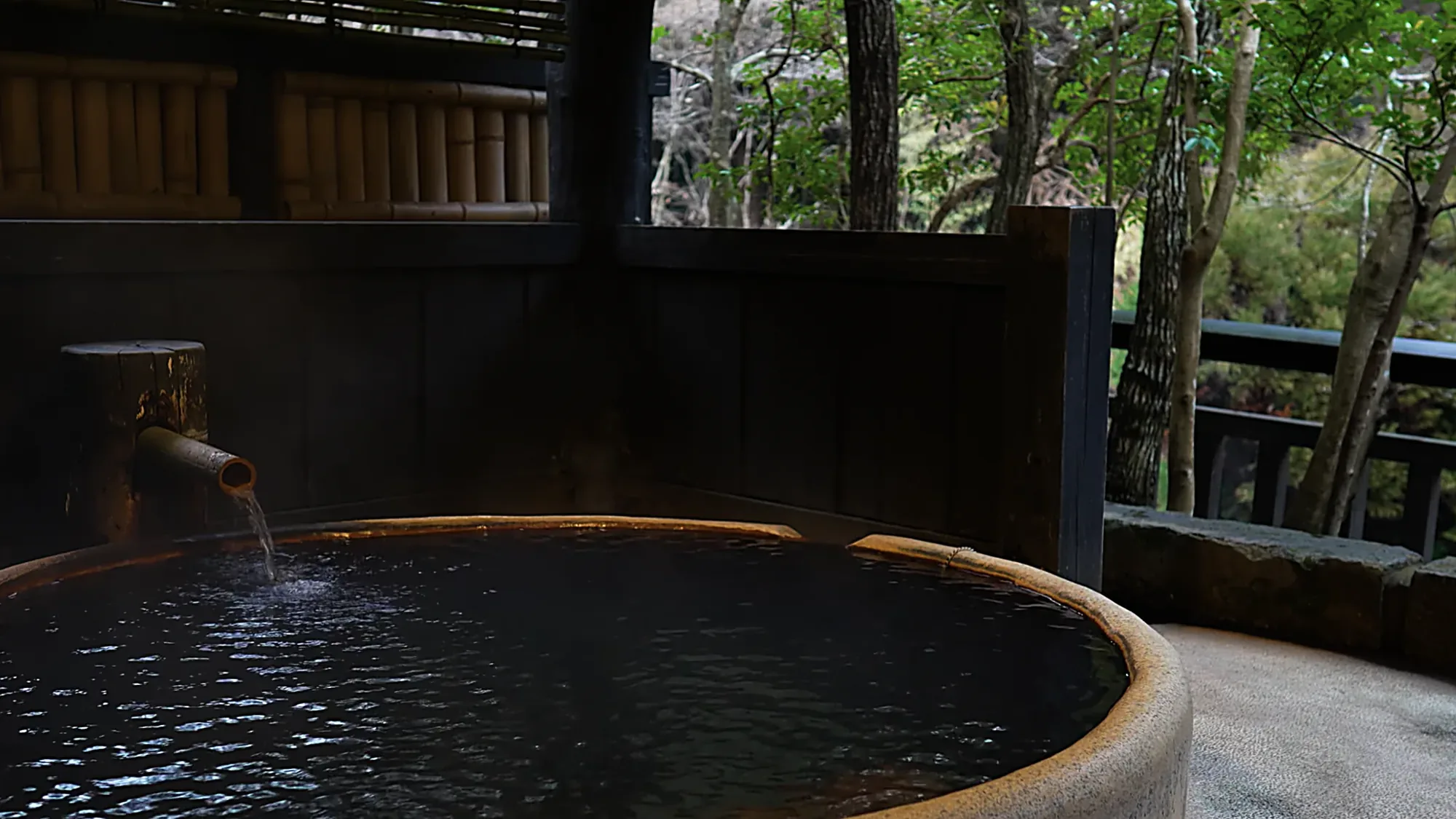 A bathing tub at Kurokawa Onsen behind a bamboo screen, forest filling the frame