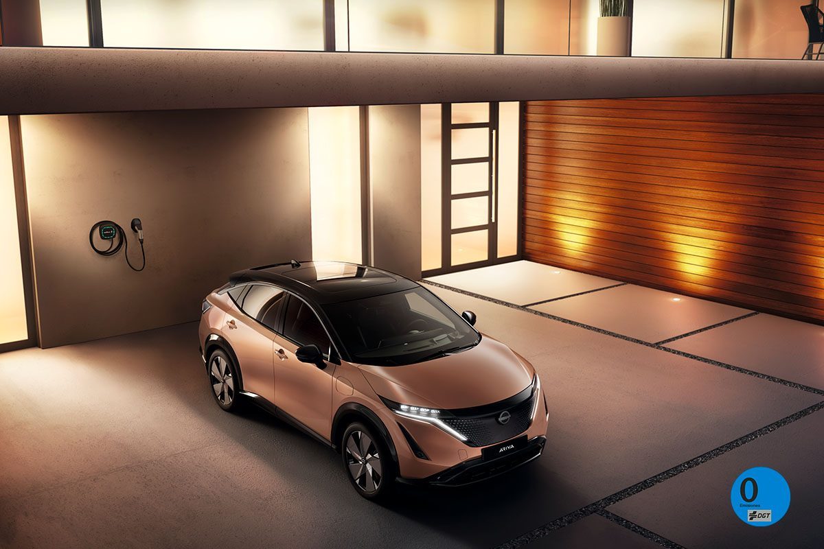 "Técnico de Citroën sonriendo mientras revisa un vehículo blanco con detalles rojos, en un taller con neumáticos al fondo."