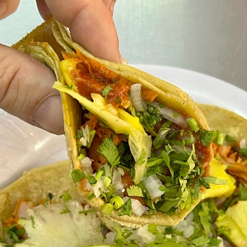 Kamay na may hawak na bagung-bagong taco al pastor na puno ng marinated na baboy, pinya, tinadtad na sibuyas, at cilantro.