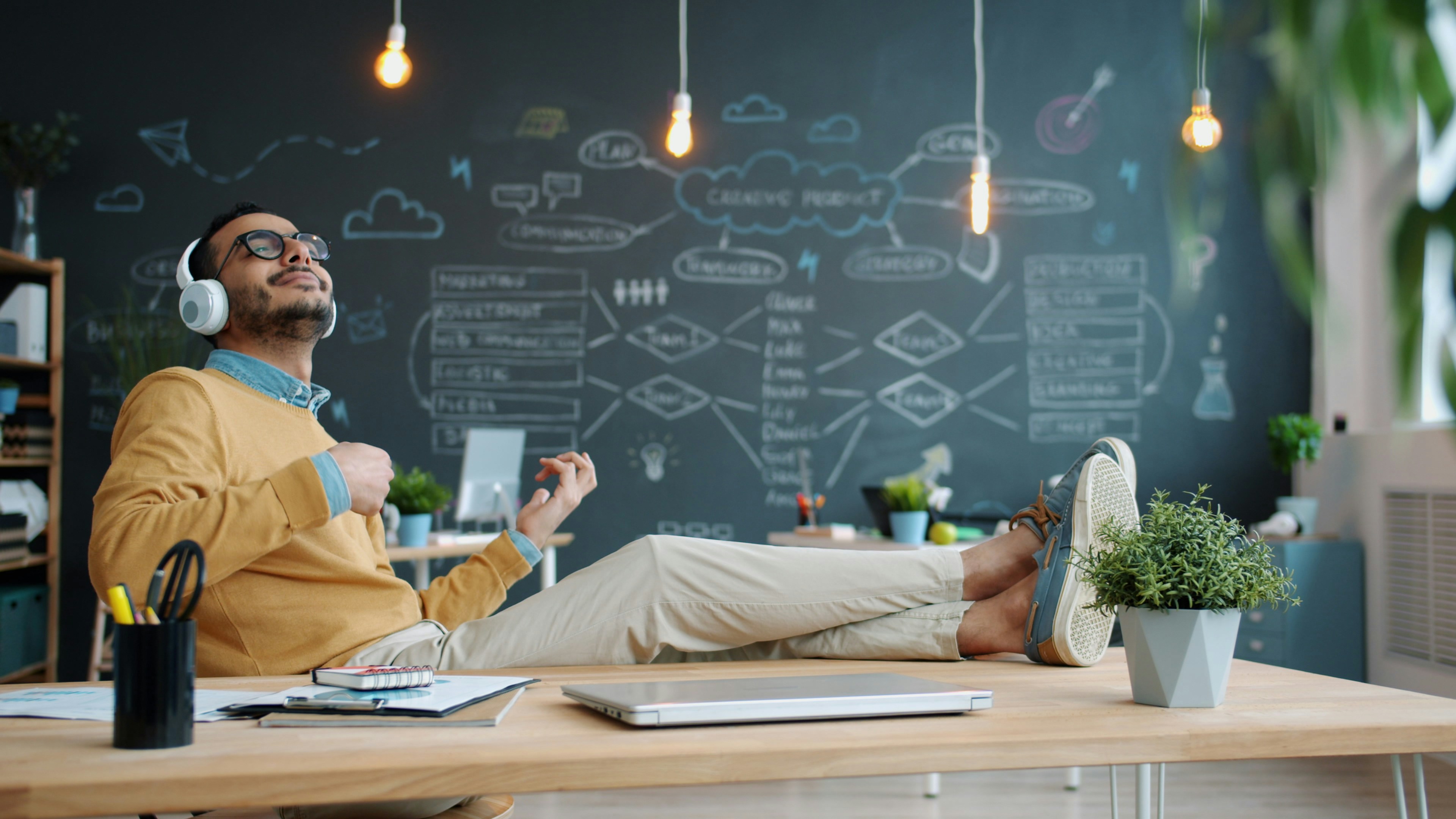 Man wearing headphones plays air guitar at desk