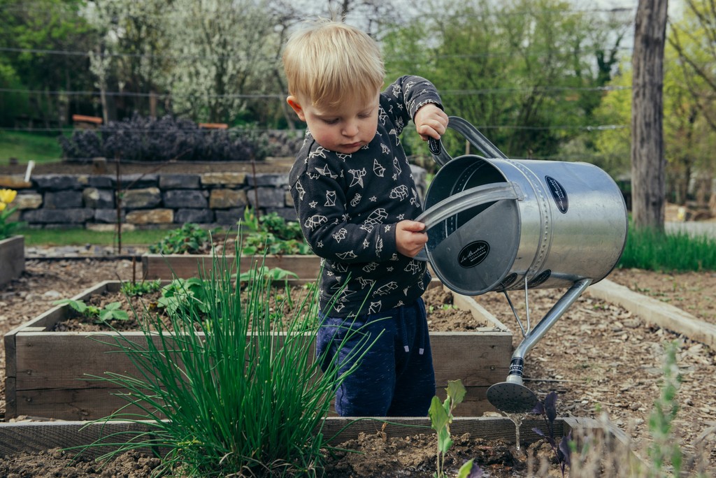 Een klein kindje die water geeft aan een tuin van Intergreen Tuinen