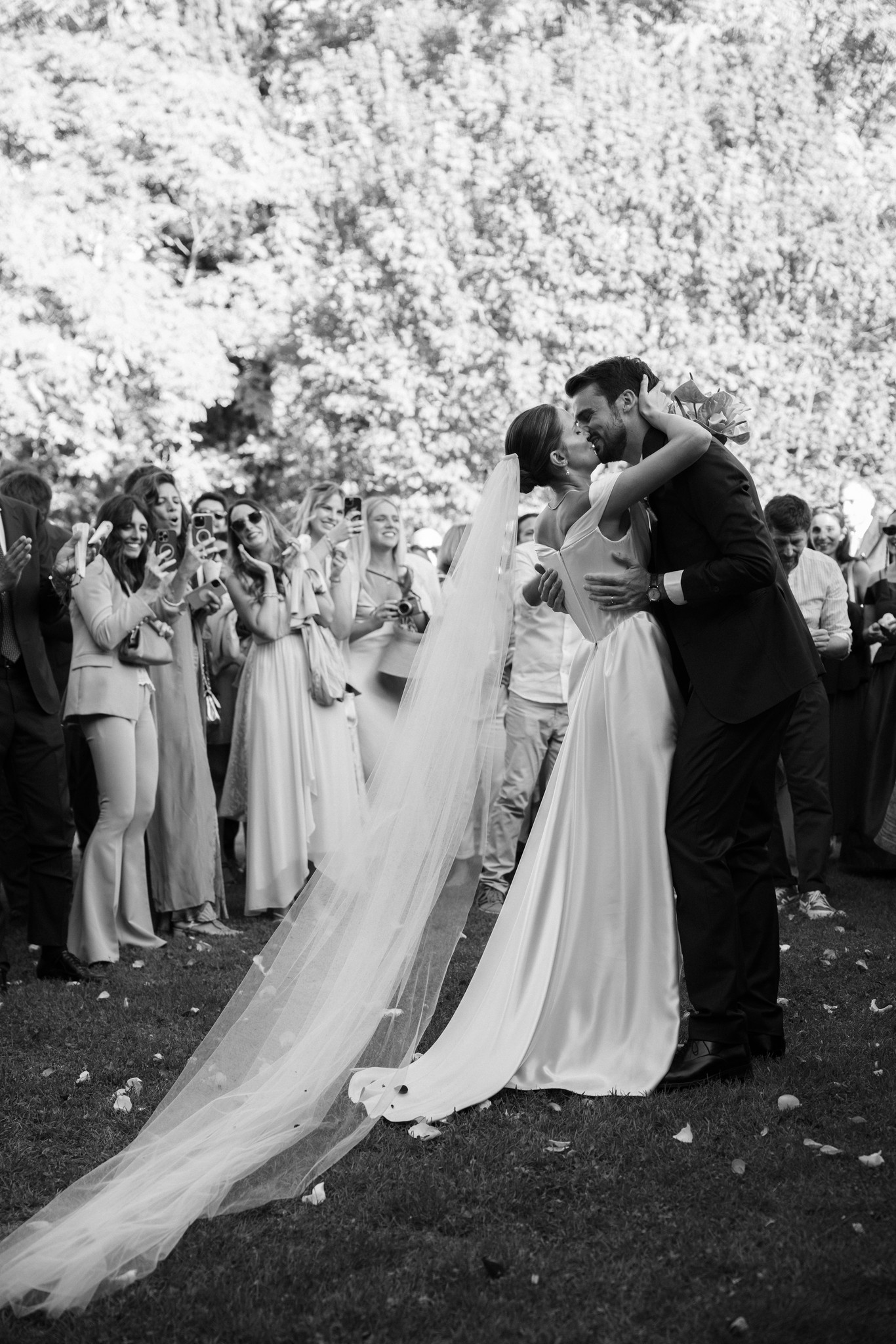 Sposi si baciano al Castello di Scipione circondati da invitati, velo che svolazza, cerimonia matrimoniale in bianco e nero