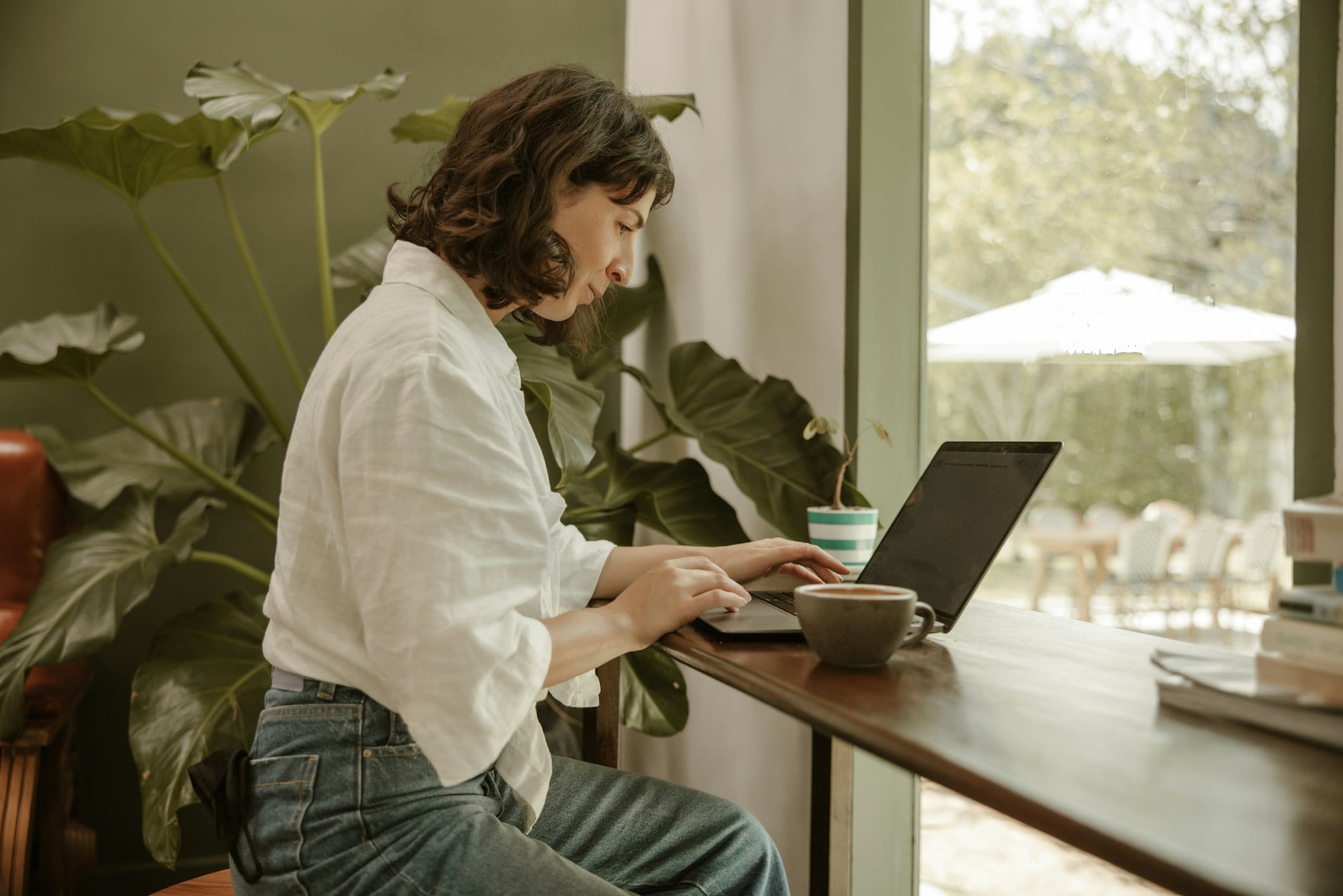 Woman working on laptop near window with plants, symbolizing mindfulness and inner balance