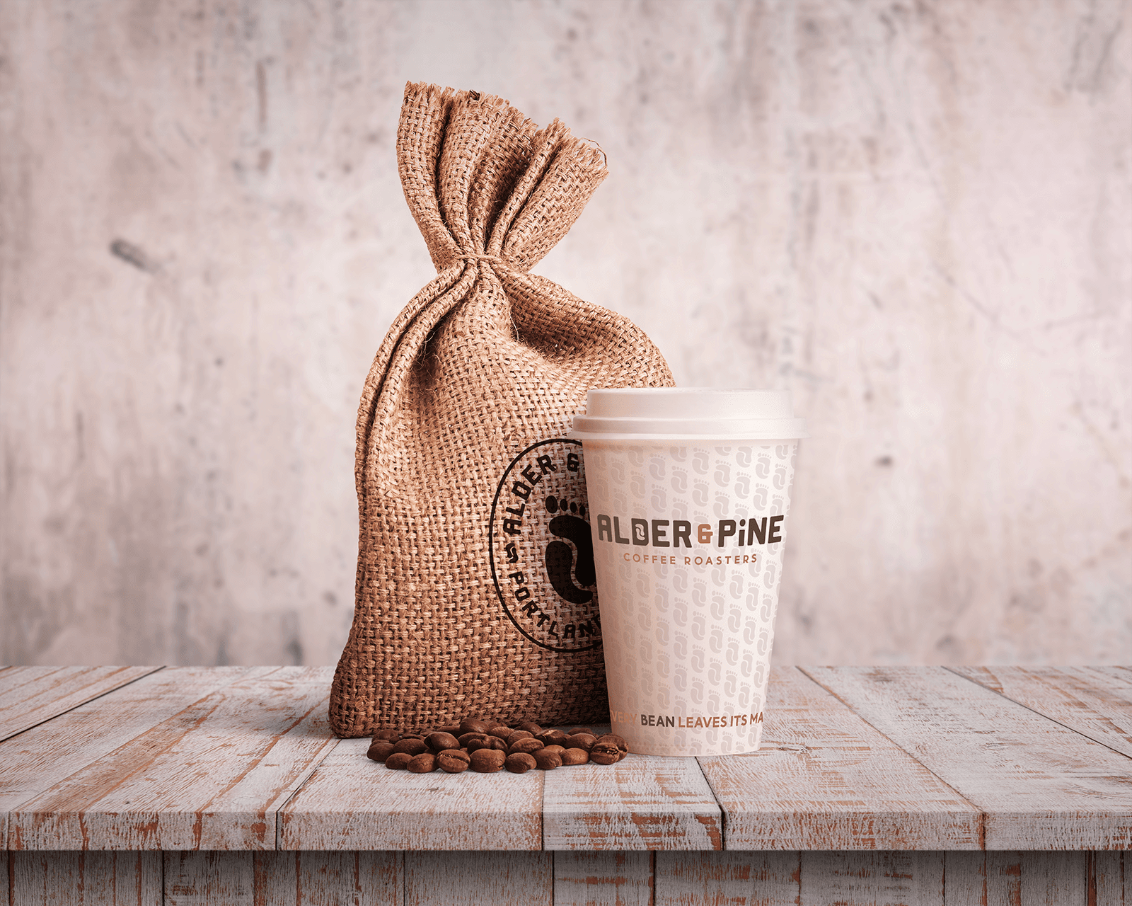 Graphic design mockup of a coffee cup and coffee bean bag for Alder & Pine Coffee Roasters — modern, clean wordmark and badge style logo of a footprint and a coffee bean with a bold decorative sans serif typography, designed by Will Lefkovich.