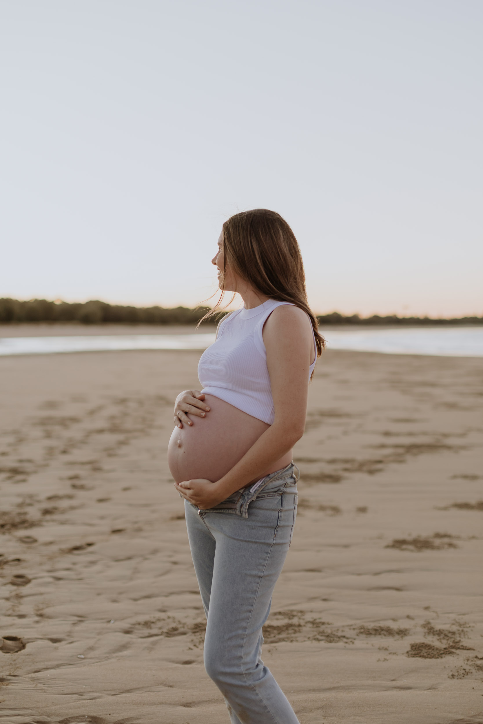 Pregnant woman having a moment with her baby bump at the beach at sunset