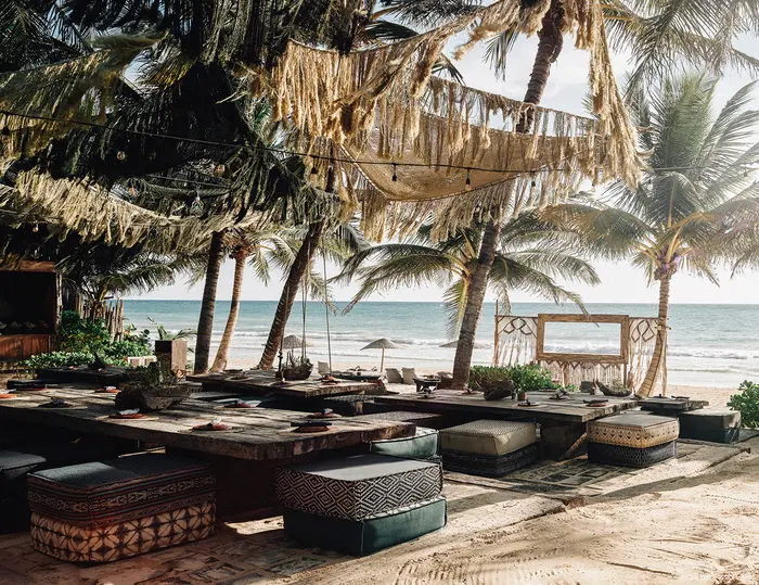 View from La Popular restaurant in Nômade Tulum, Mexico, featuring tables and chairs for dining and relaxation, surrounded by palm trees with a jungle-style and ocean view.