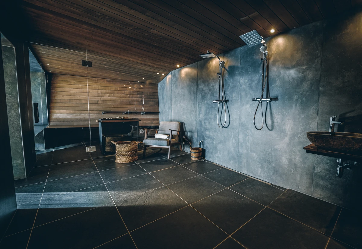 Saunavorraum mit Betonwand, Regendusche, Sessel und schwarzen Bodenfliesen