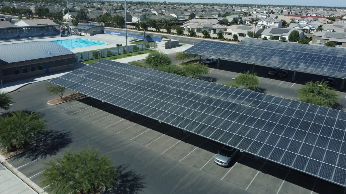 Drone view of solar carports over a parking lot next to a pool and homes in Bakersfield, CA