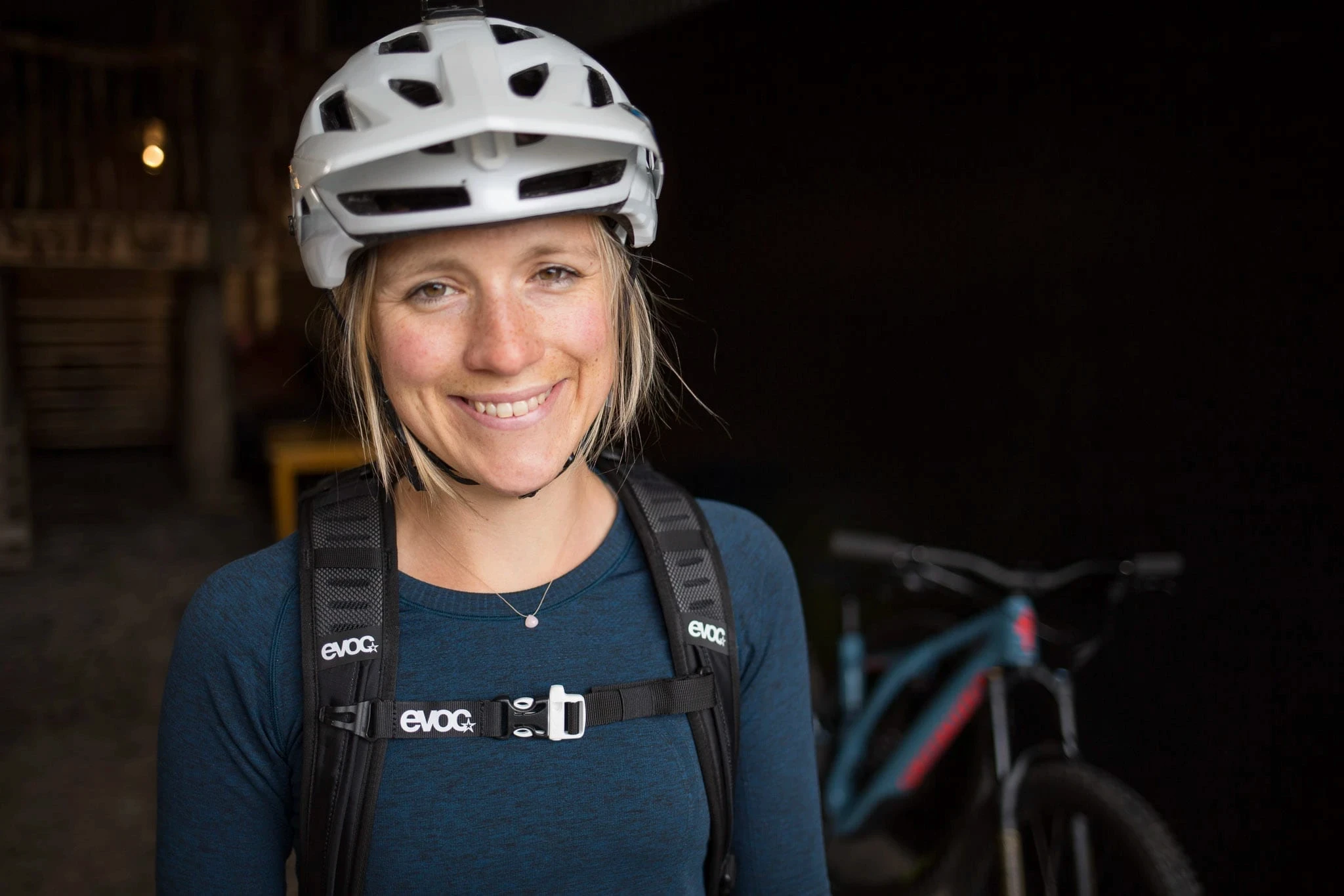 Smiling cyclist wearing a helmet and backpack, with a bike in the background.