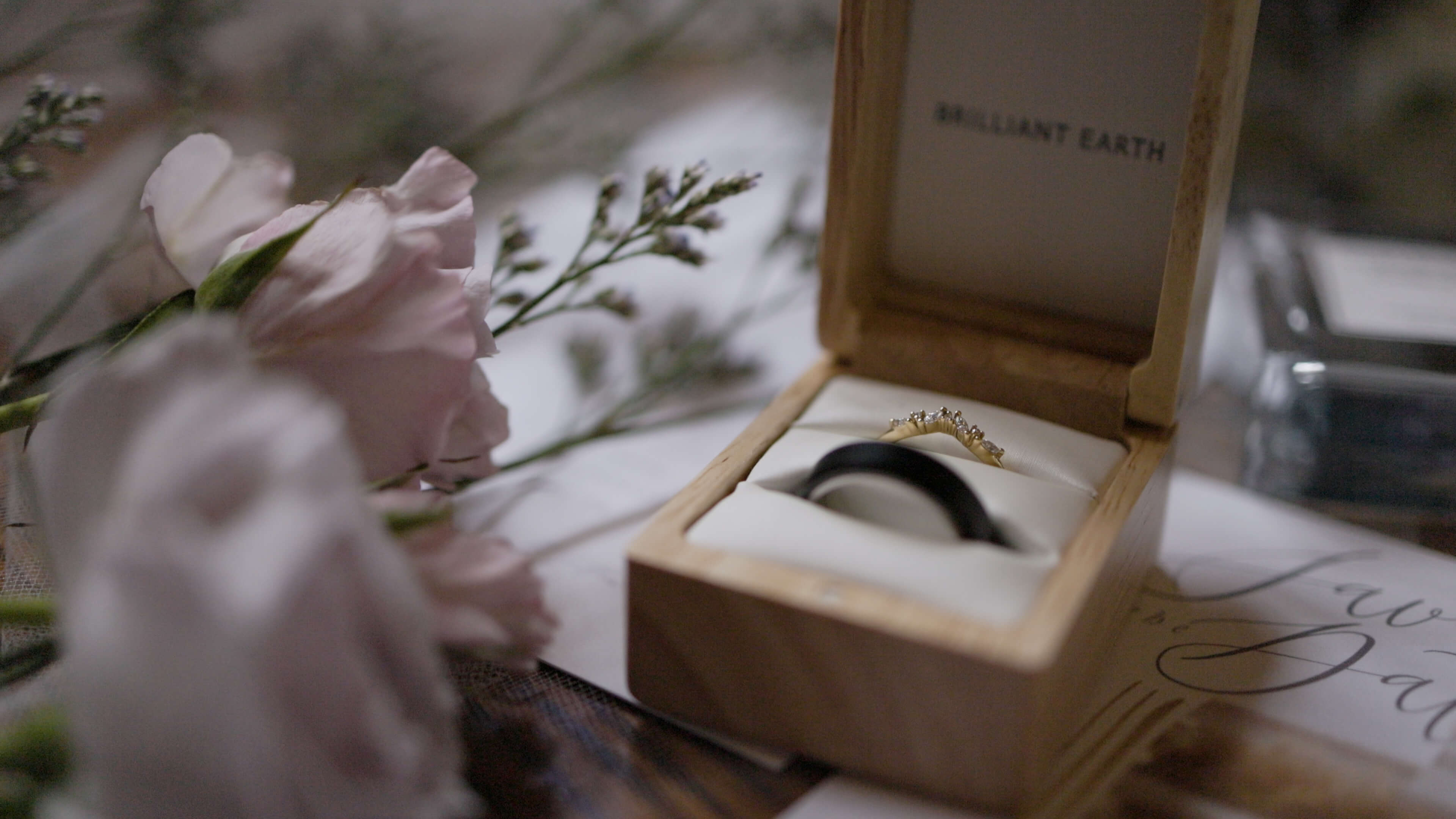 Wedding rings in a wooden box next to pink flowers