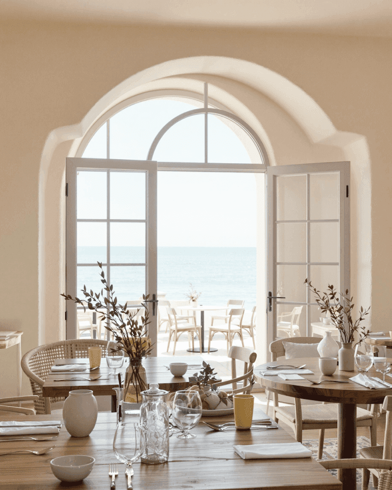 Elegant seaside restaurant with wooden tables and ocean view through arched doors.