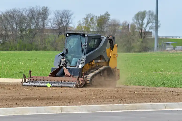 Skid steer workig in a field with a harley rank attachment