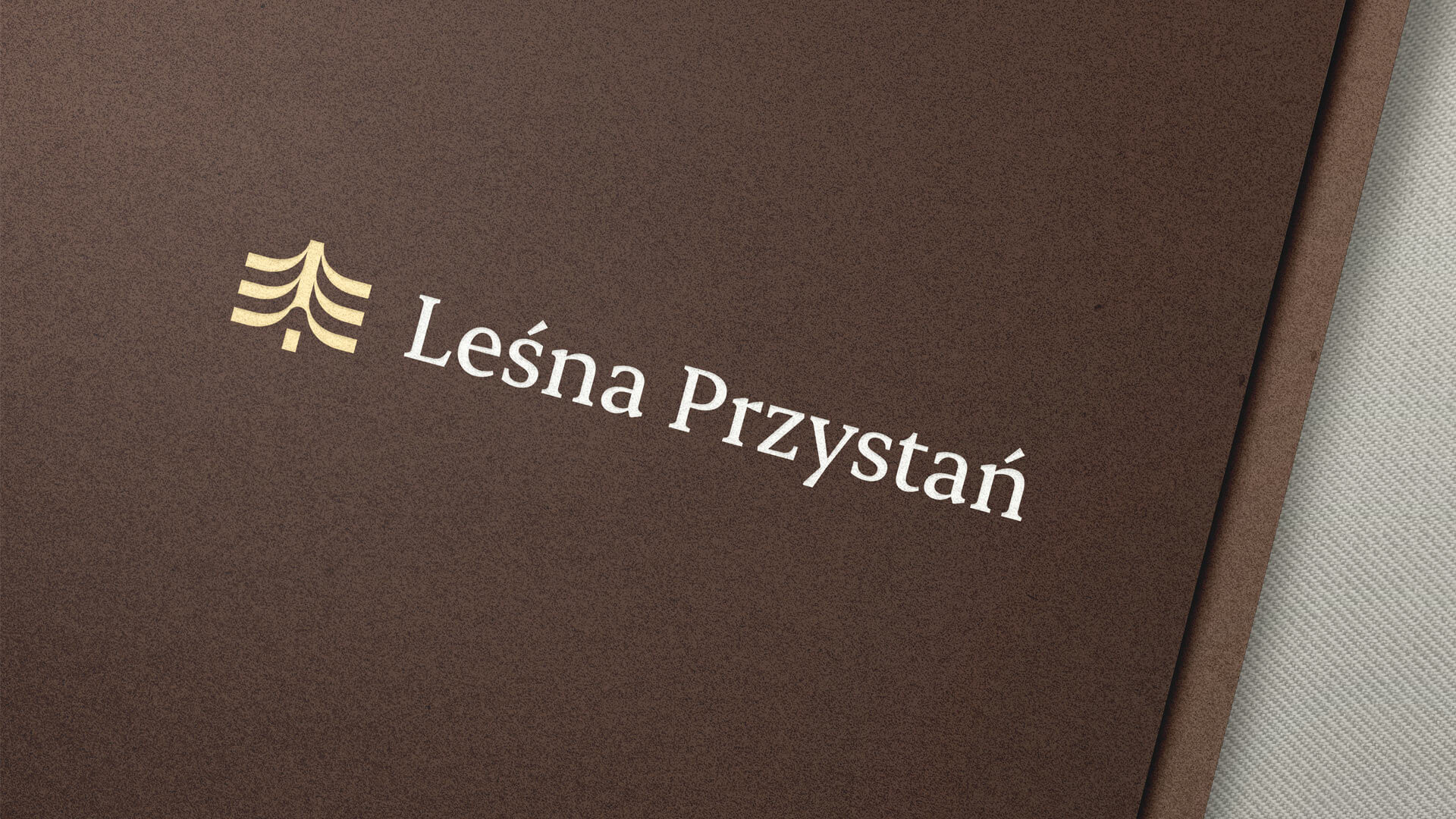 Brązowa, teksturowana okładka menu, na której widnieje tekst „Leśna Przystań” w eleganckiej białej czcionce obok stylizowanego logo przedstawiającego złote drzewo, nawiązuje do rustykalnej estetyki i natury.