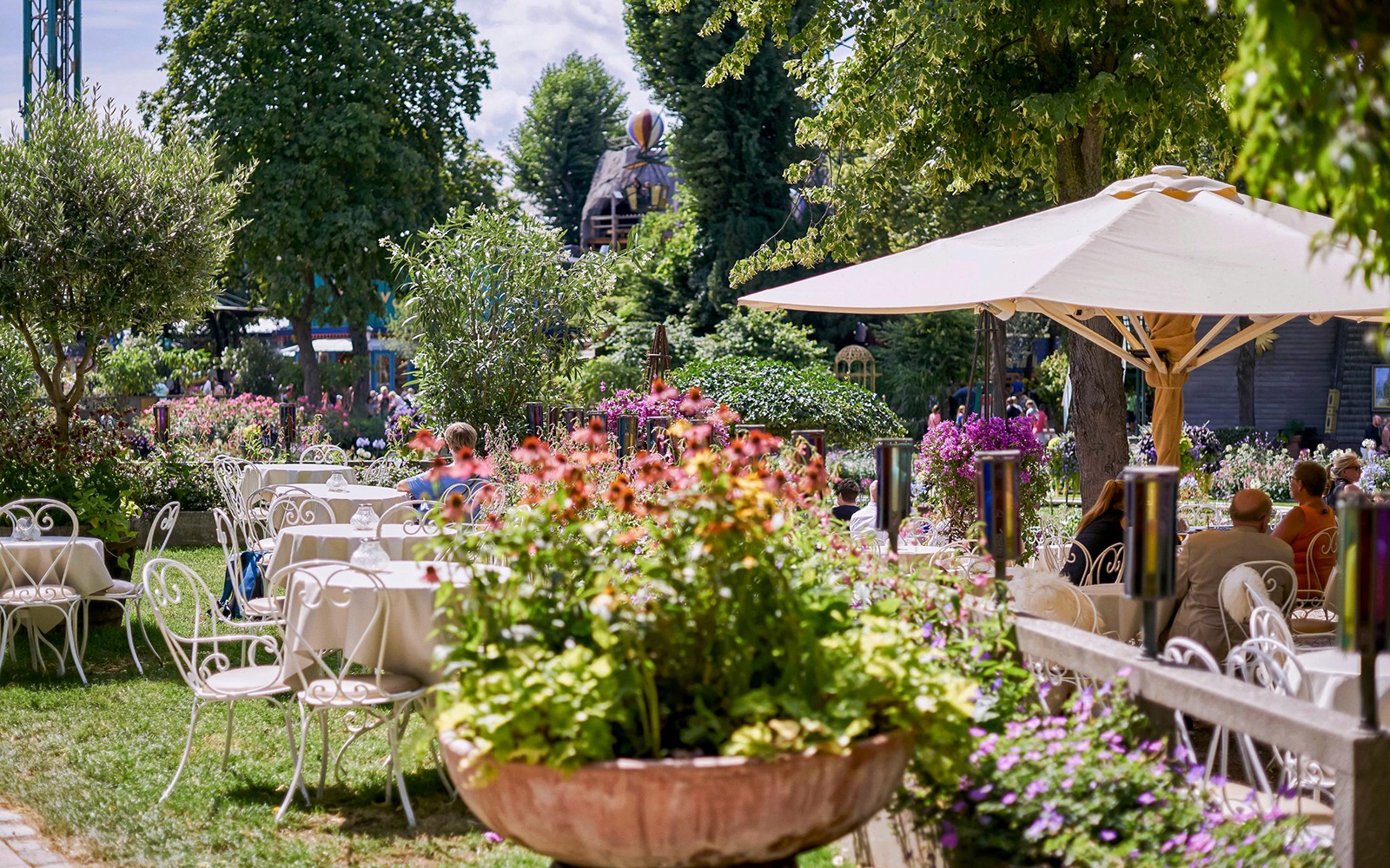 Tivoli Kertekben található kültéri étkezőhelyiség, amelyet virágok vesznek körül, és asztalokkal és székekkel van berendezve.