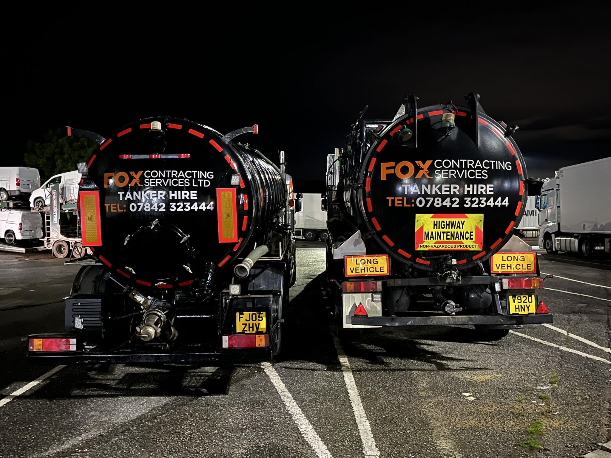 Two Fox Contracting Services vacuum tankers parked at night, viewed from the rear with high-visibility branding and phone numbers on the tanks.