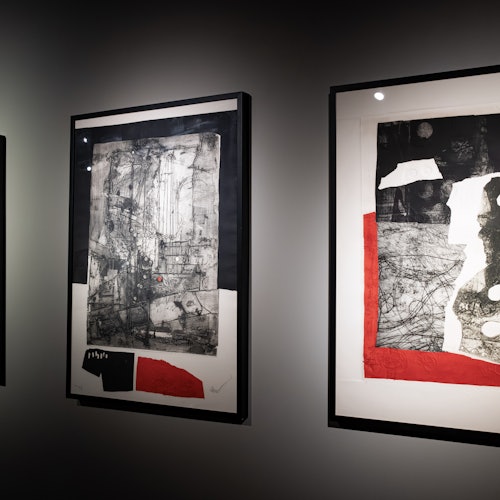 Ang mga nakakahon na abstraktong sining na tampok ang mga kulay na pula, itim, at puti ay nakasabit sa isang madilim na naiilawang kulay abong pader sa isang galerya.