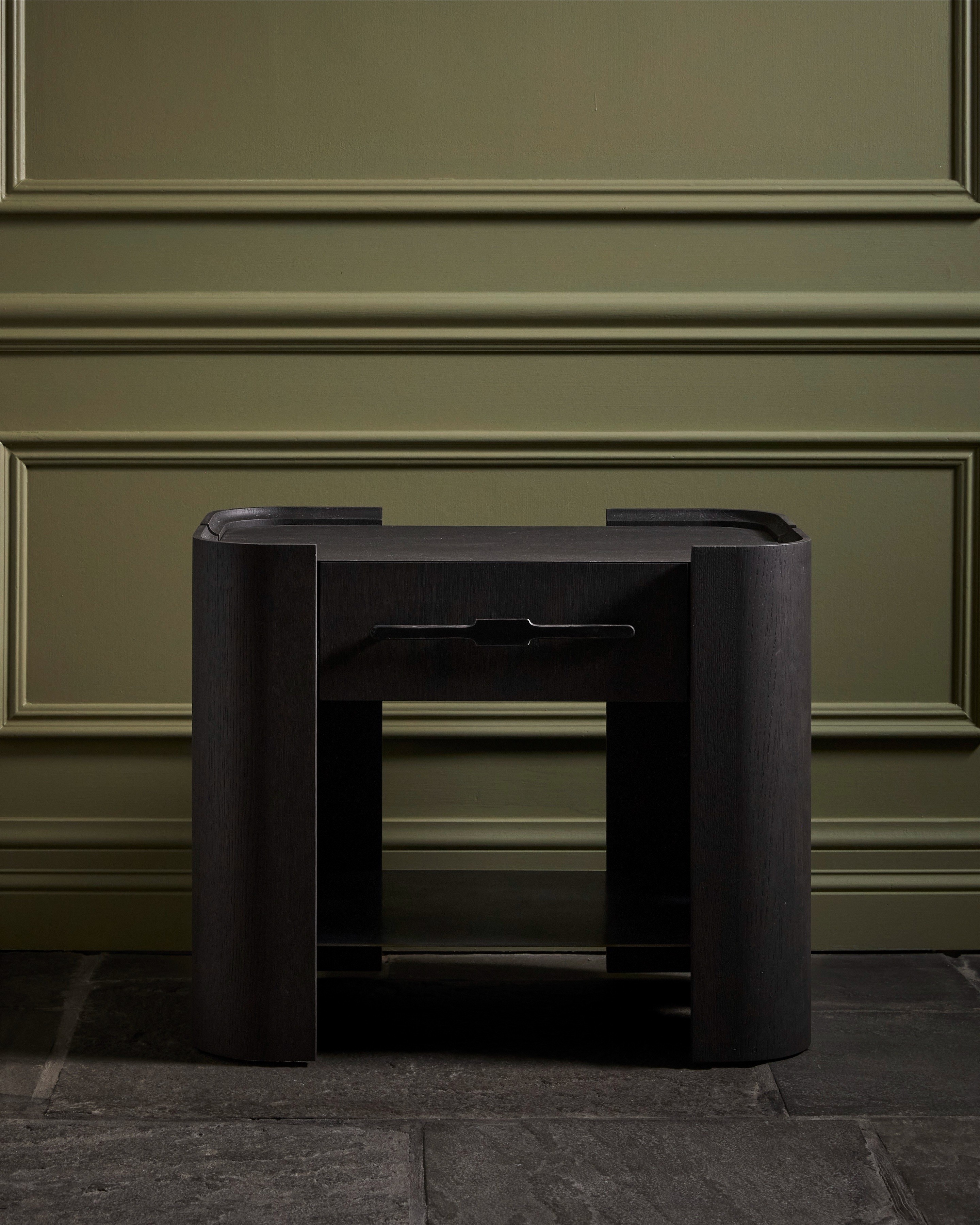 A Willow Collection nightstand in black-stained oak against olive panelling