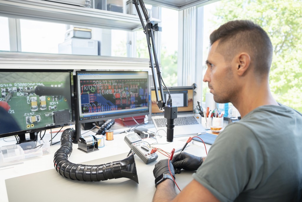 A person sits at a desk with dual monitors, focused on work, in a well-lit, modern office space.