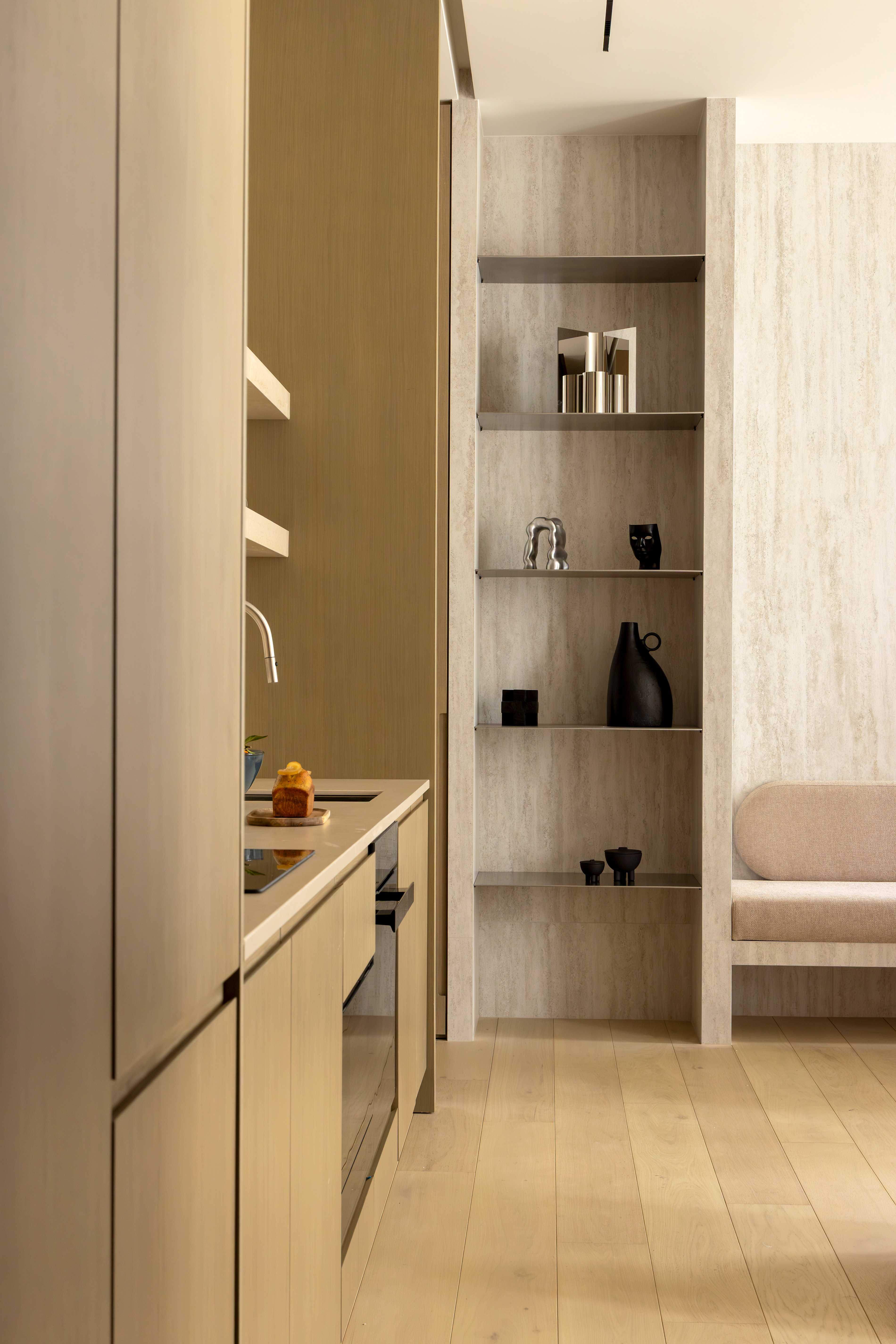 Detail cuisine en bois clair avec evier, etageres en travertin et objets decoratifs noirs sur niches