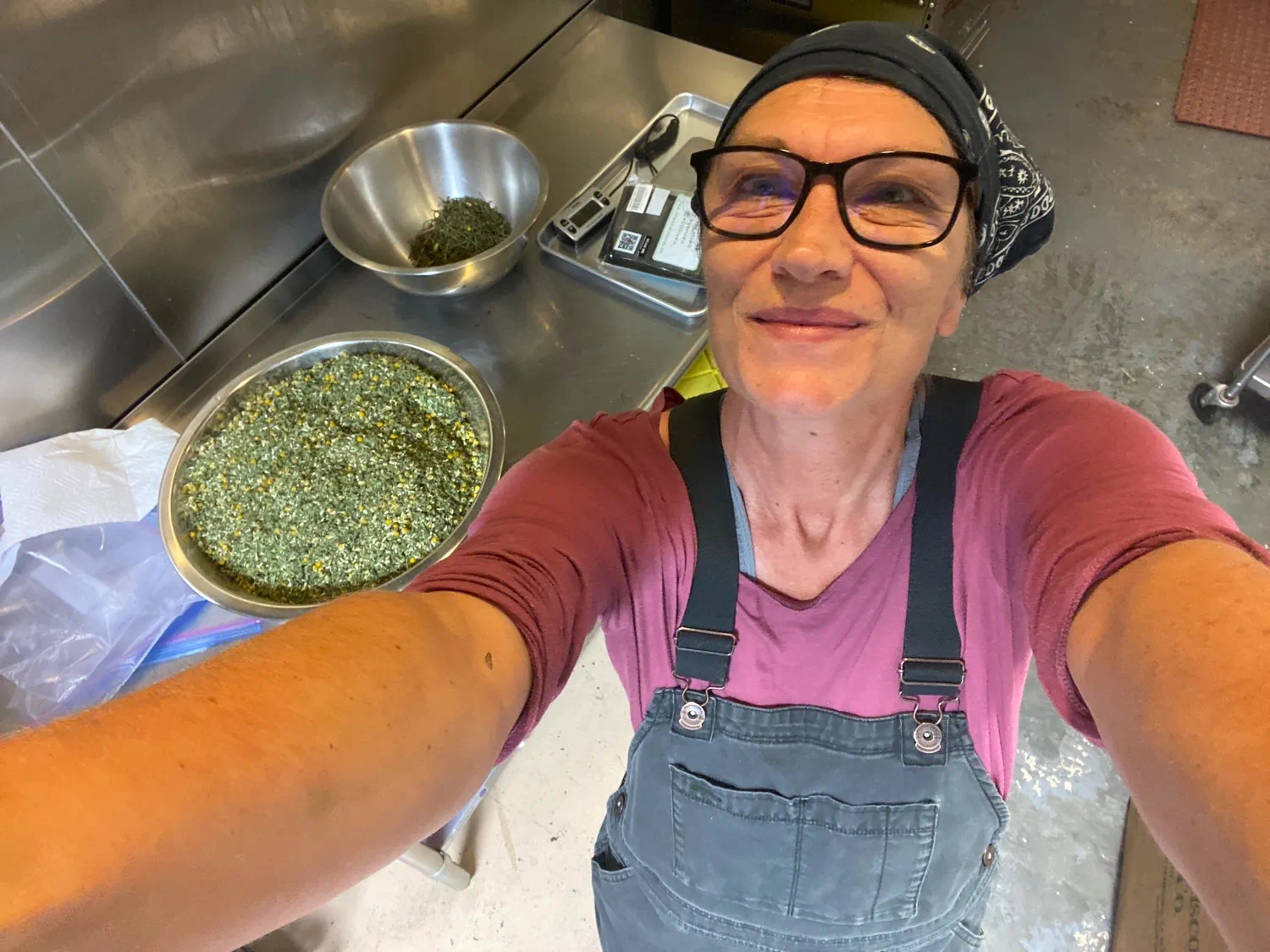 A woman smiling while preparing loose-leaf herbal tea in a commercial kitchen.