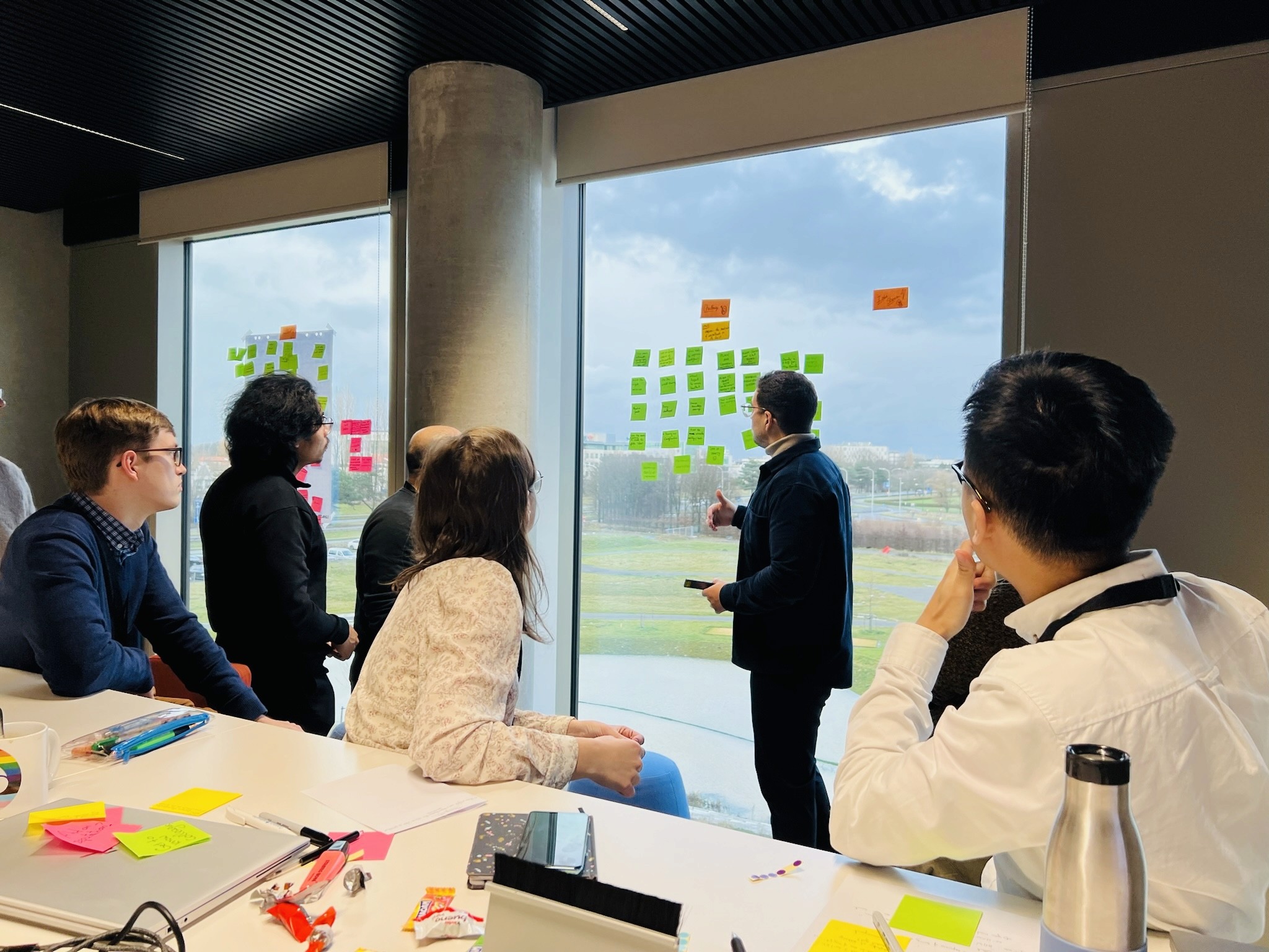 Team participating in a facilitation workshop, discussing and placing sticky notes on a window during a collaborative session in Belgium
