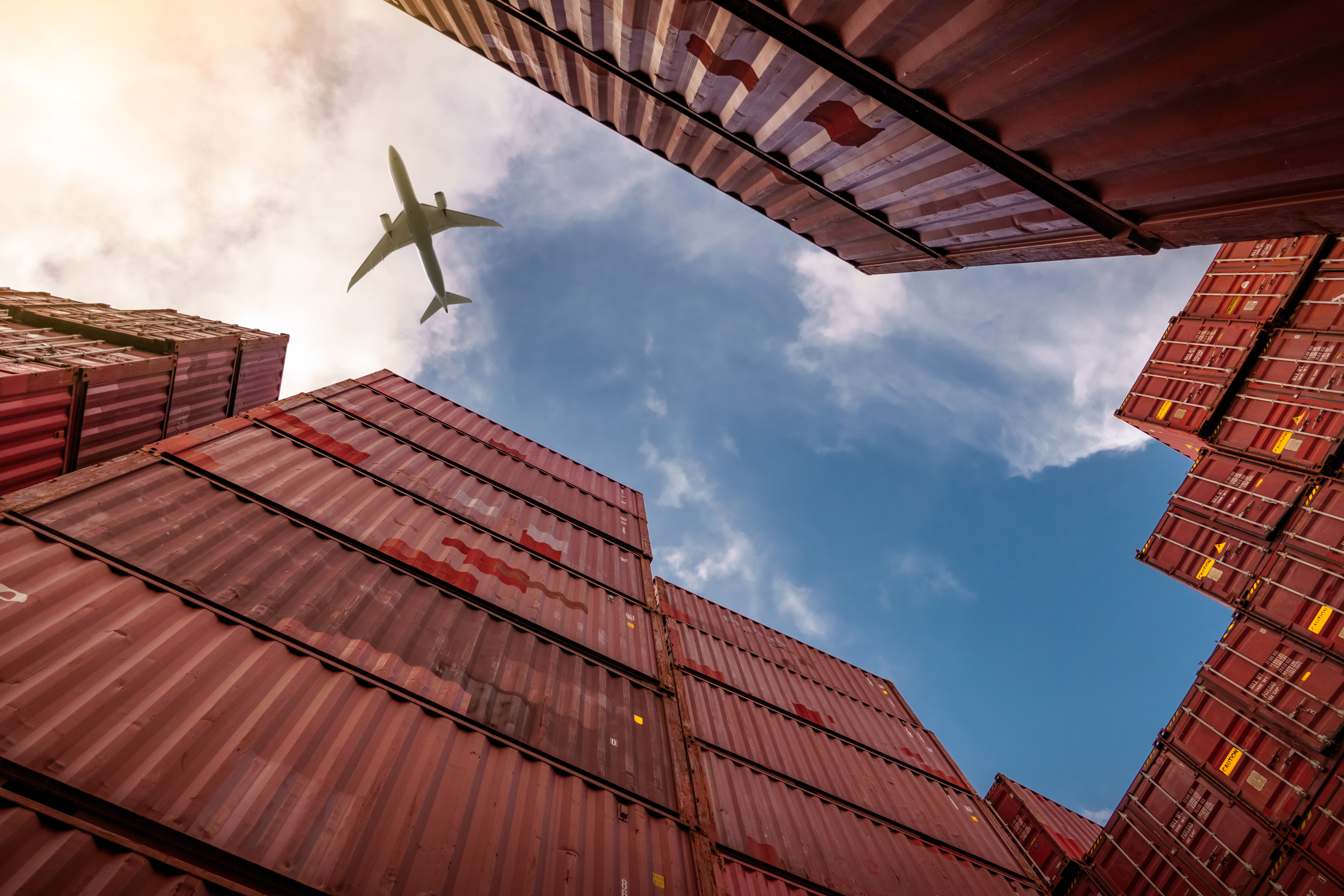 An aeroplane flies over shipping containers used for imports and exports