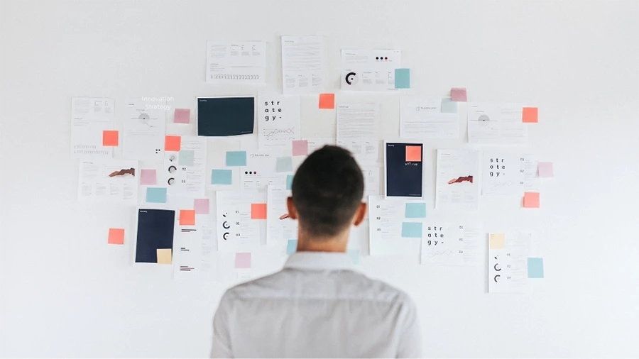 Person standing in front of whiteboard looking at it. Whiteboard has sticky notes and other notes on it.