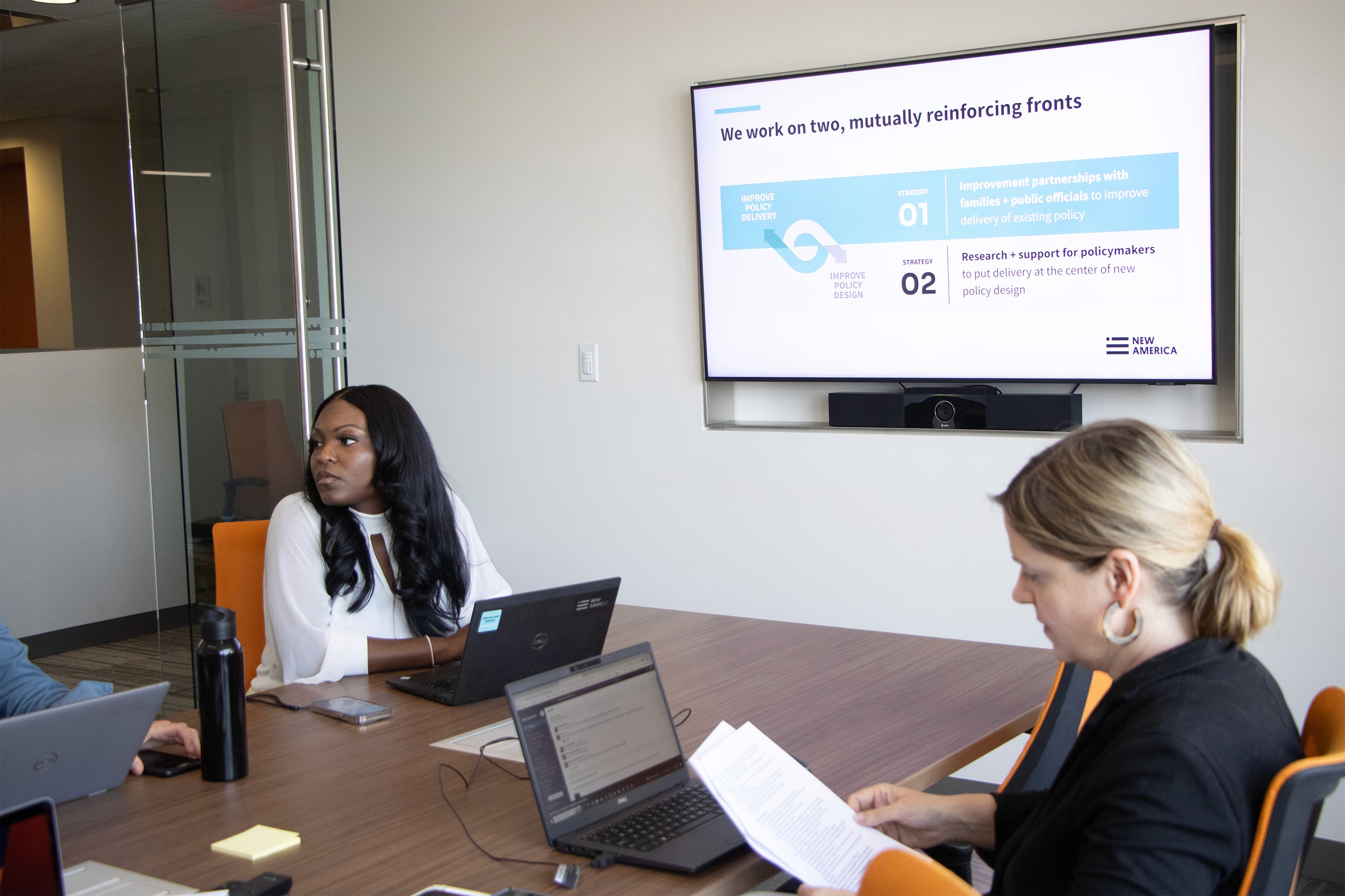 Two woman in a conference room setting, having a meeting with their laptops open on the table.