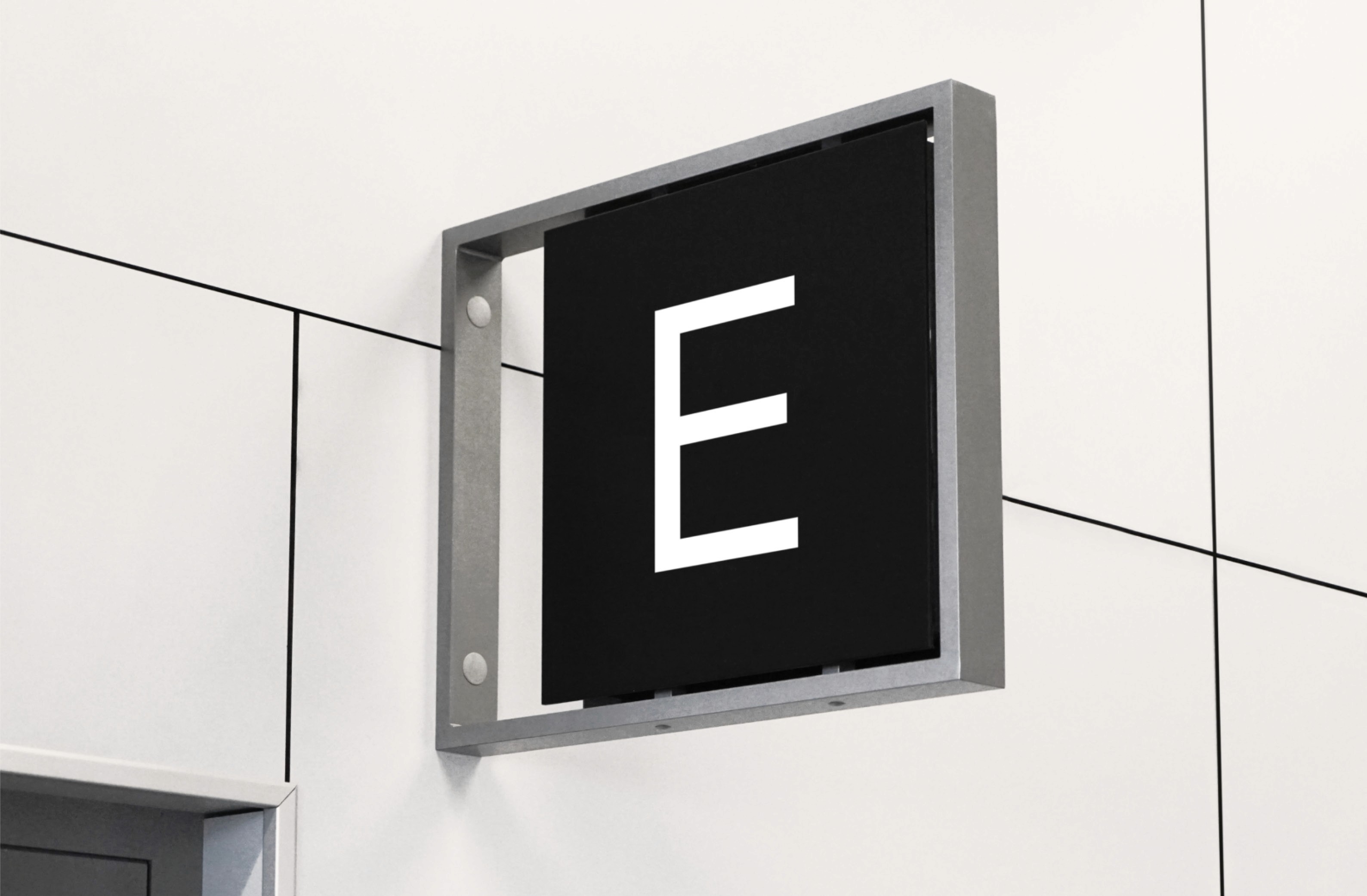 Signboard displaying the letter "E" against a black background in a minimalist interior setting.