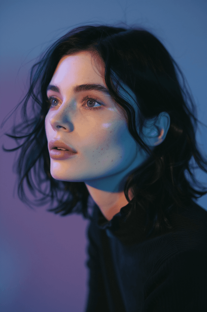 A woman with dark hair and striking blue eyes gazes thoughtfully into the distance.