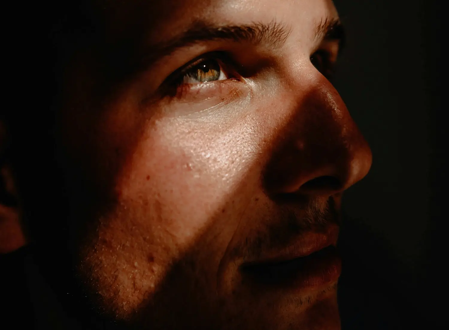 Close-up portrait of a man struggling with internalized homophobia in dramatic light and shadow, gazing upward with a reflective, introspective expression, symbolizing inner struggle and emotional healing.