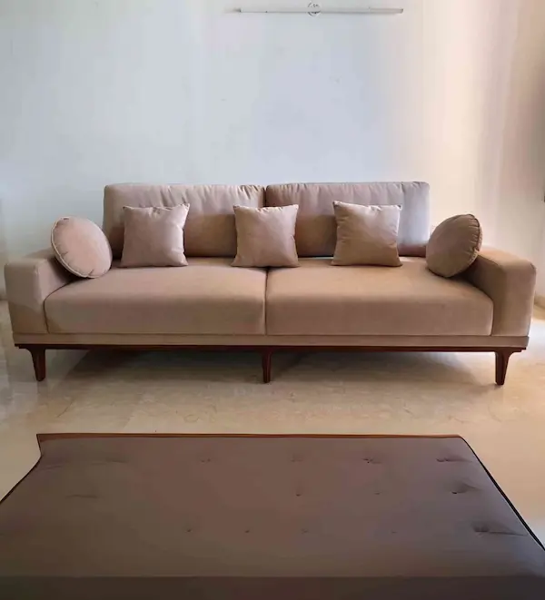 A customized beige upholstered sofa with loose cushions, bolster pillows, and wooden legs