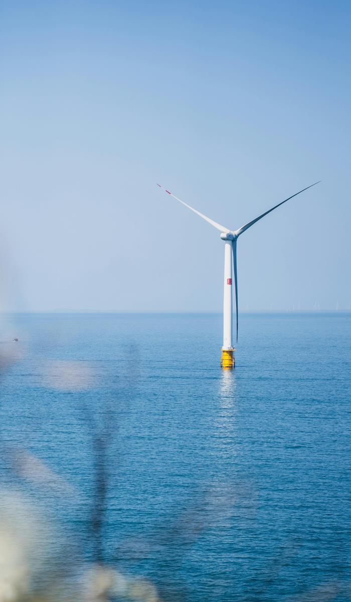 Wind turbine standing alone in a calm blue sea under a clear sky. The serene setting conveys a sense of tranquility and sustainable energy.